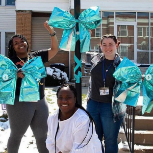Three young people putting up large teal ribbons on a lamppost