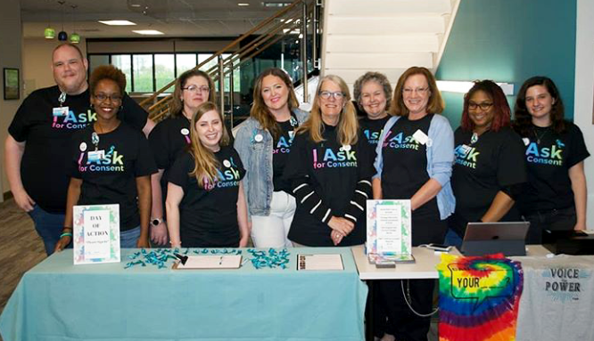 A group of individuals stand in front of their SAAM table at their Day of Action event.