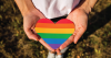 Person holding a heart that is painted in the colors of the rainbow flag