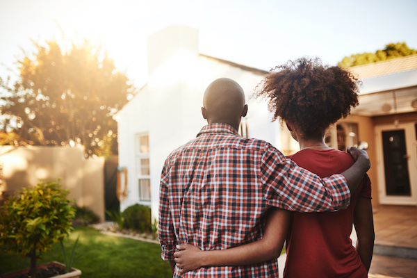 A black man and woman with arms around each other, facing the sun