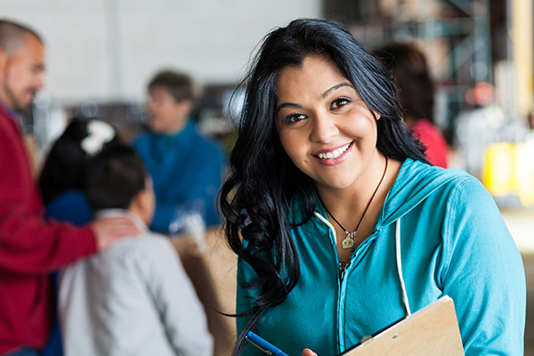 Woman smiling wearing a teal hoodie and holding a clipboard