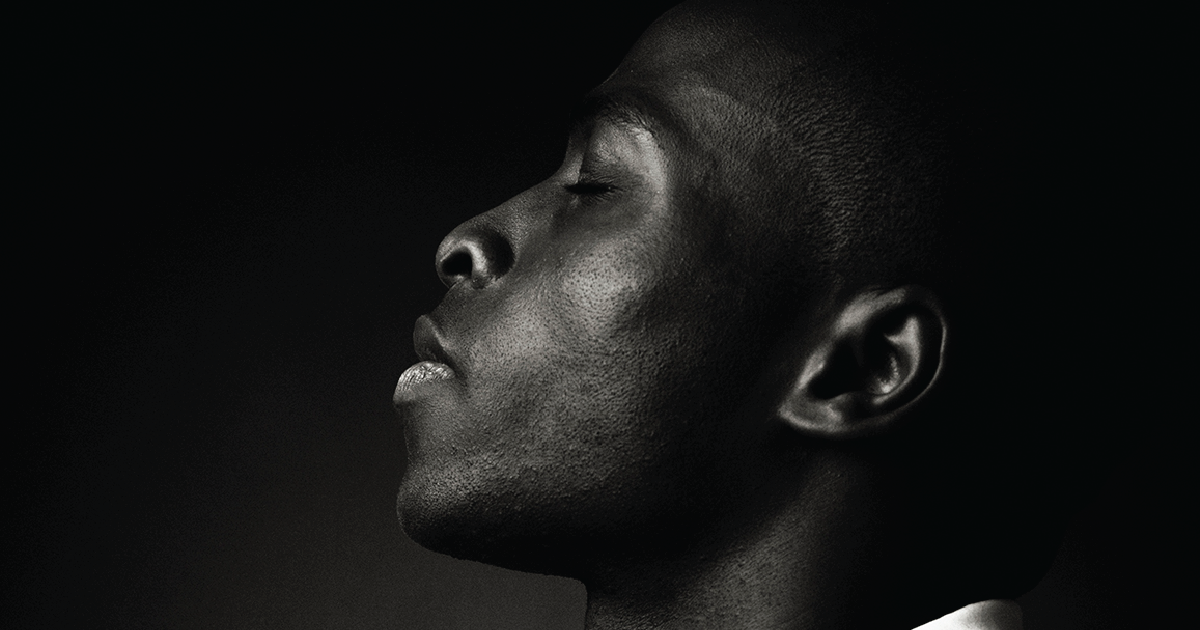 Black man in profile standing in front of a dark wall