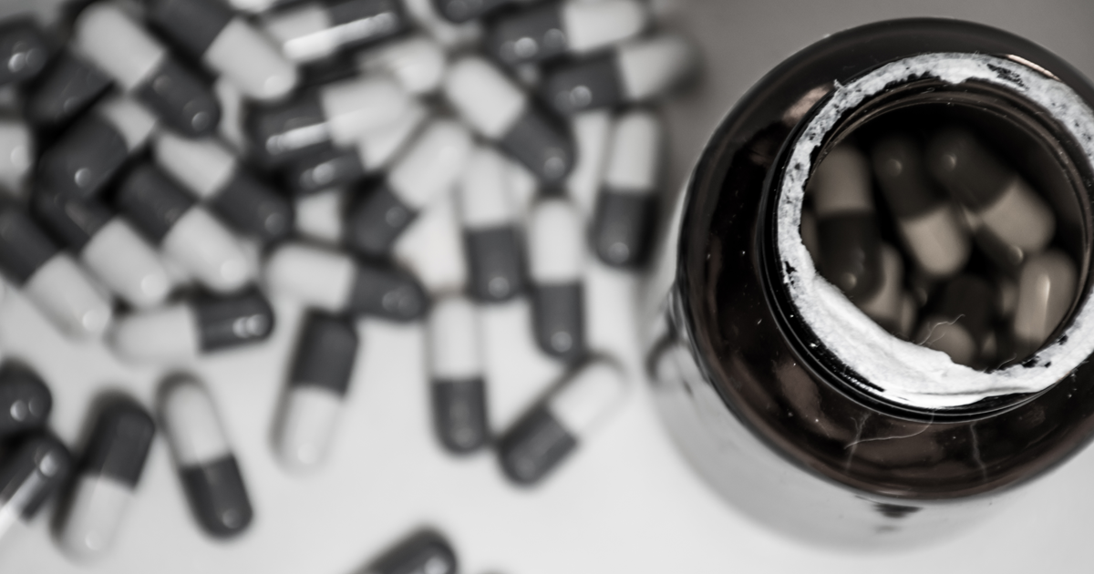 An open bottle of pills with pills lying on the table beside it