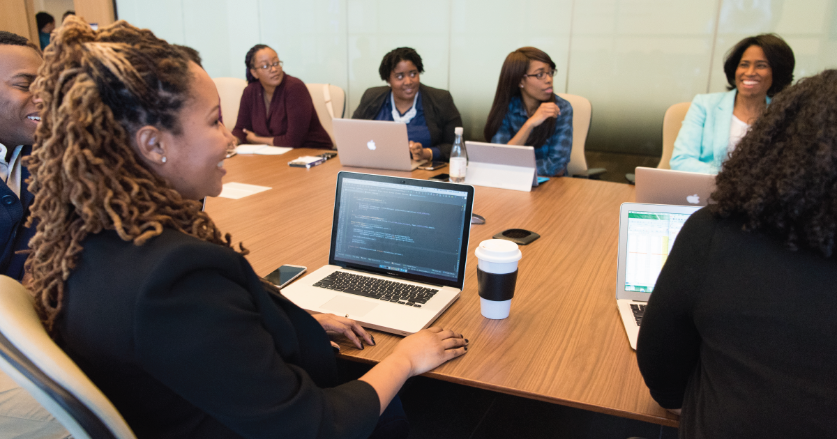 A team of people of color sitting around a conference table with laptops