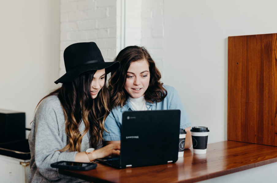 Two women sit at a laptop, talking.