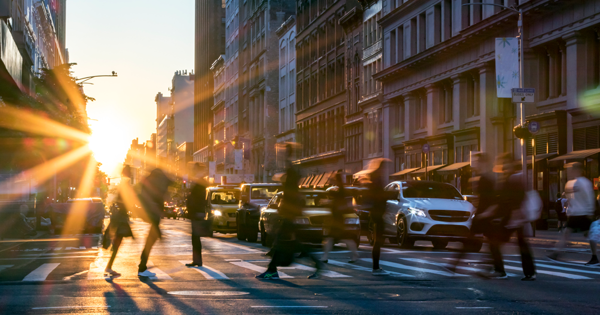 a group of people crossing the street at sunrise