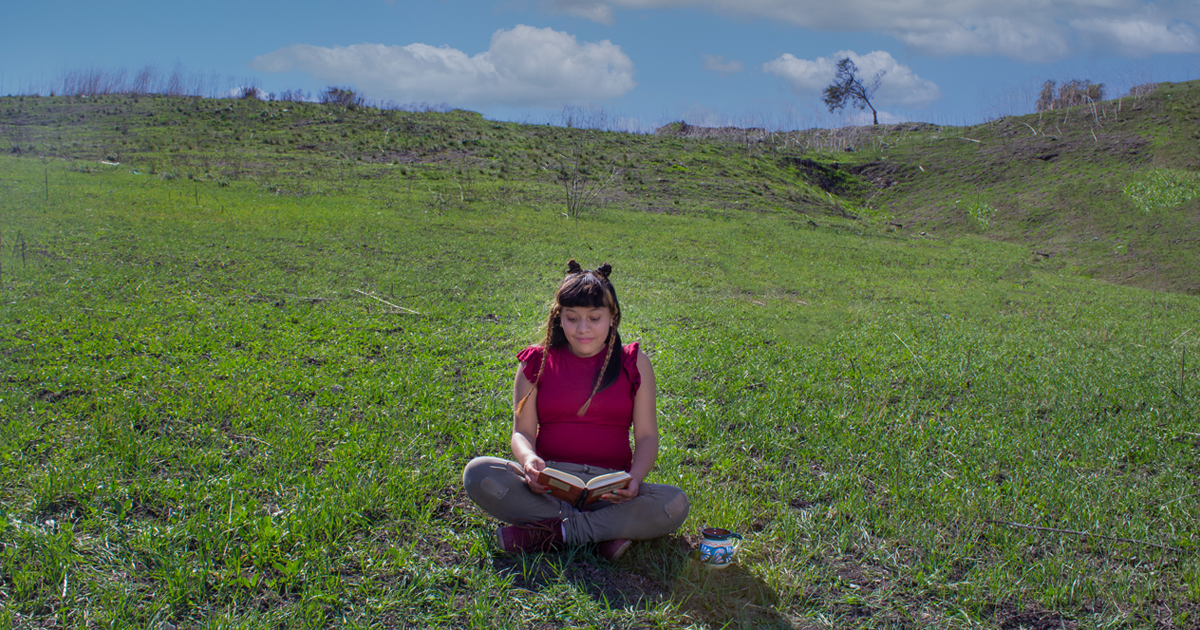 Girl sitting on the grass outside, smiling and reading a book