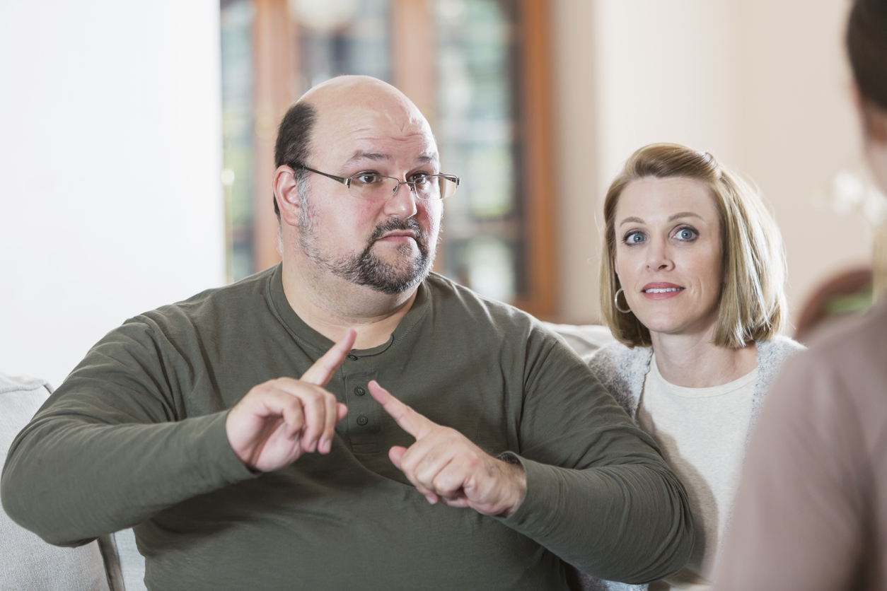 image of two people, one is signing to a third person off screen.