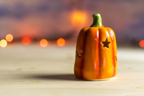 a ceramic pumpkin with stars carved out is in the foreground, with orange Halloween lights in the background.