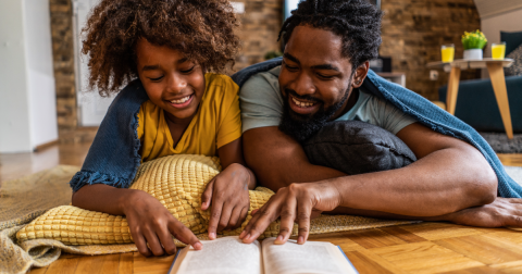 Black father and daughter reading a book together