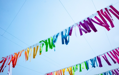 Blue sky with rainbow colored strips of paper hanging as decoration in the air like streamers