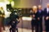 Image of a video camera pointing a people in the unfocused background