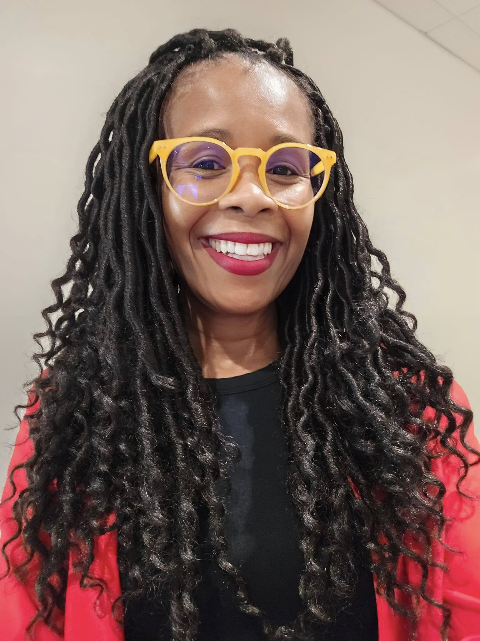 A Black woman in yellow glasses and red blazer smiling at the camera