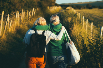 Two women walk in a field with an arm around each other.