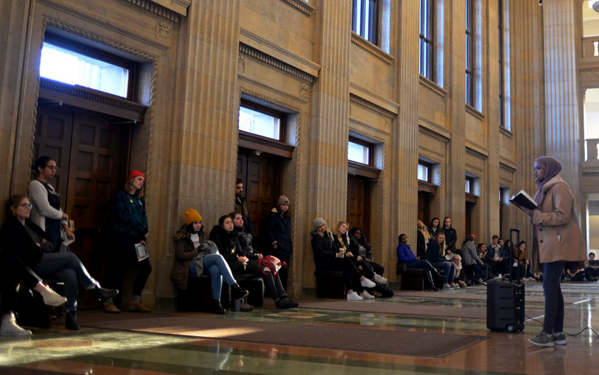 A young woman gives a speech about sexual violence to a group of students.